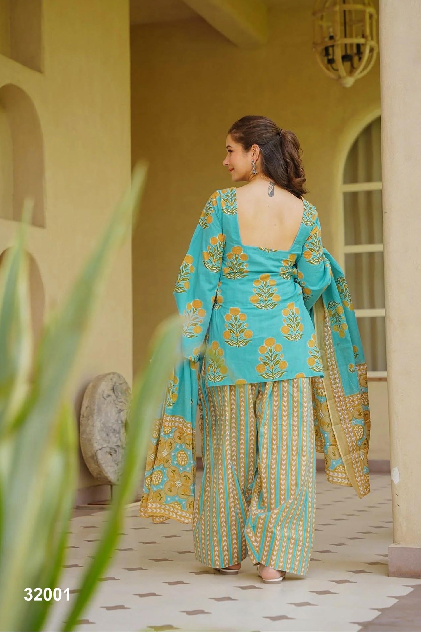 Woman in a turquoise and gold traditional outfit standing in a decorative indoor setting.