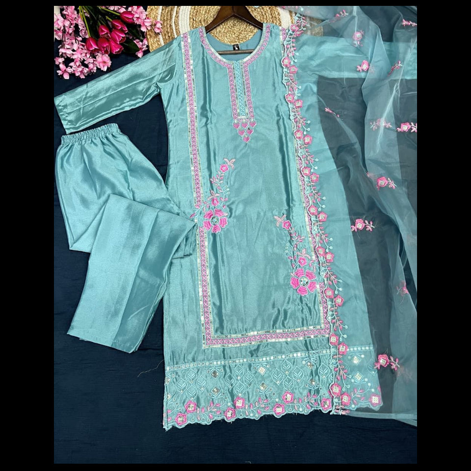 Teal embroidered outfit with pink details on a dark background