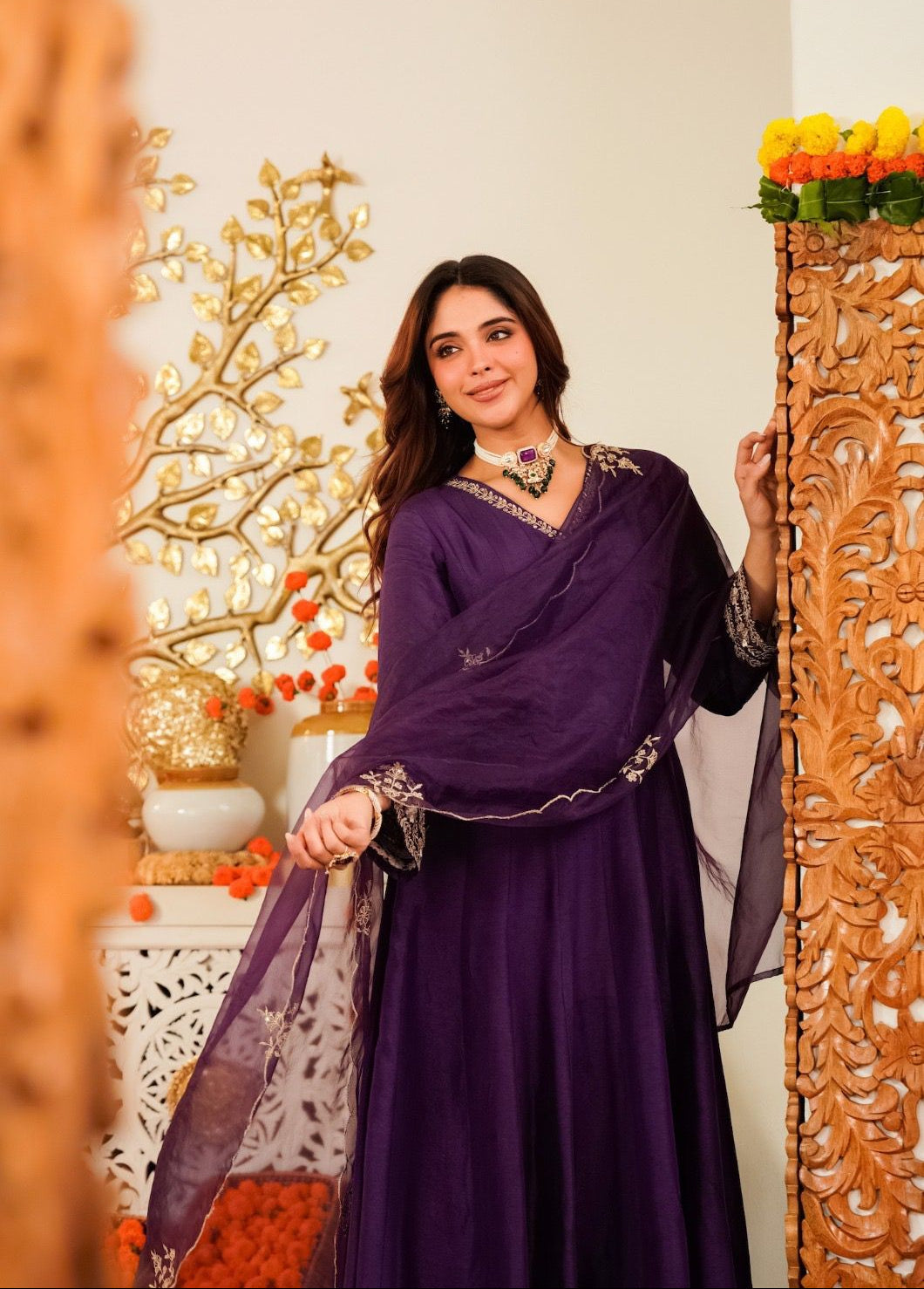 Woman in a purple traditional outfit standing next to decorative elements.