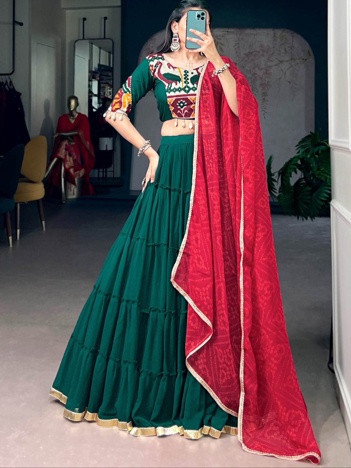 Person wearing a green and red traditional outfit with a red dupatta in a room.