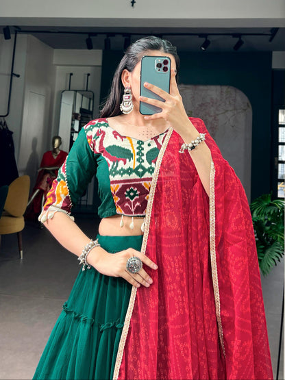 Person wearing a traditional outfit with a green and red saree in an indoor setting.