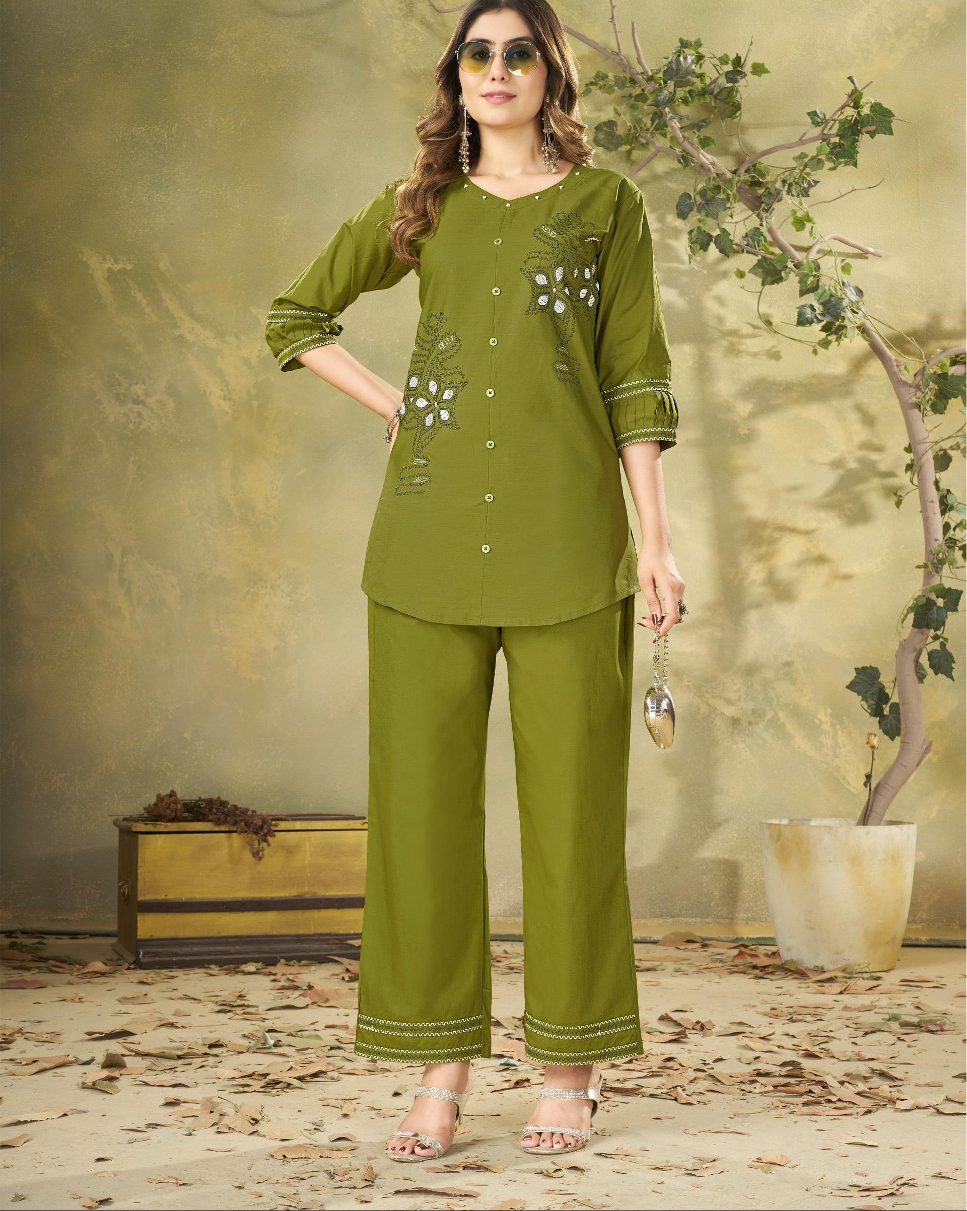 Woman wearing a green outfit with floral embroidery in a decorative setting.