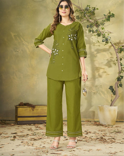 Woman wearing a green outfit with floral embroidery in a decorative setting.