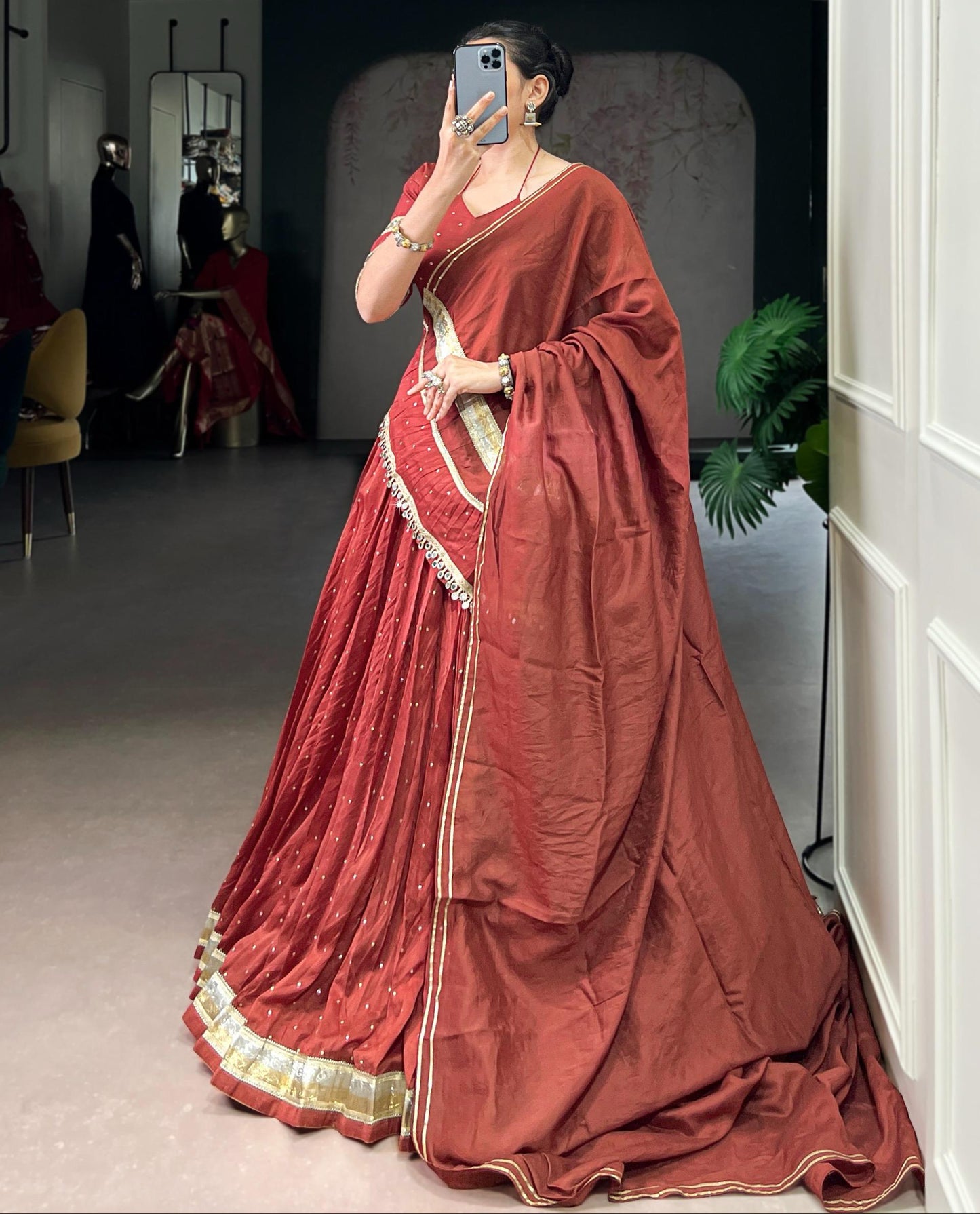 Woman in a red saree with gold border taking a mirror selfie.