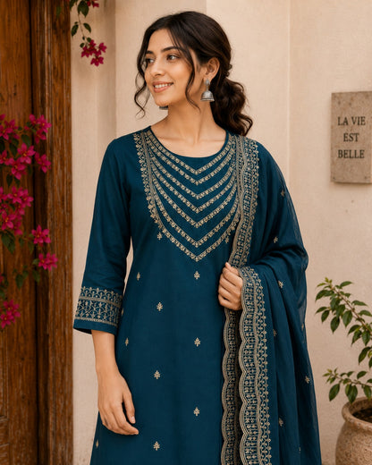 Woman wearing a blue embroidered dress standing in front of a floral door and wall.