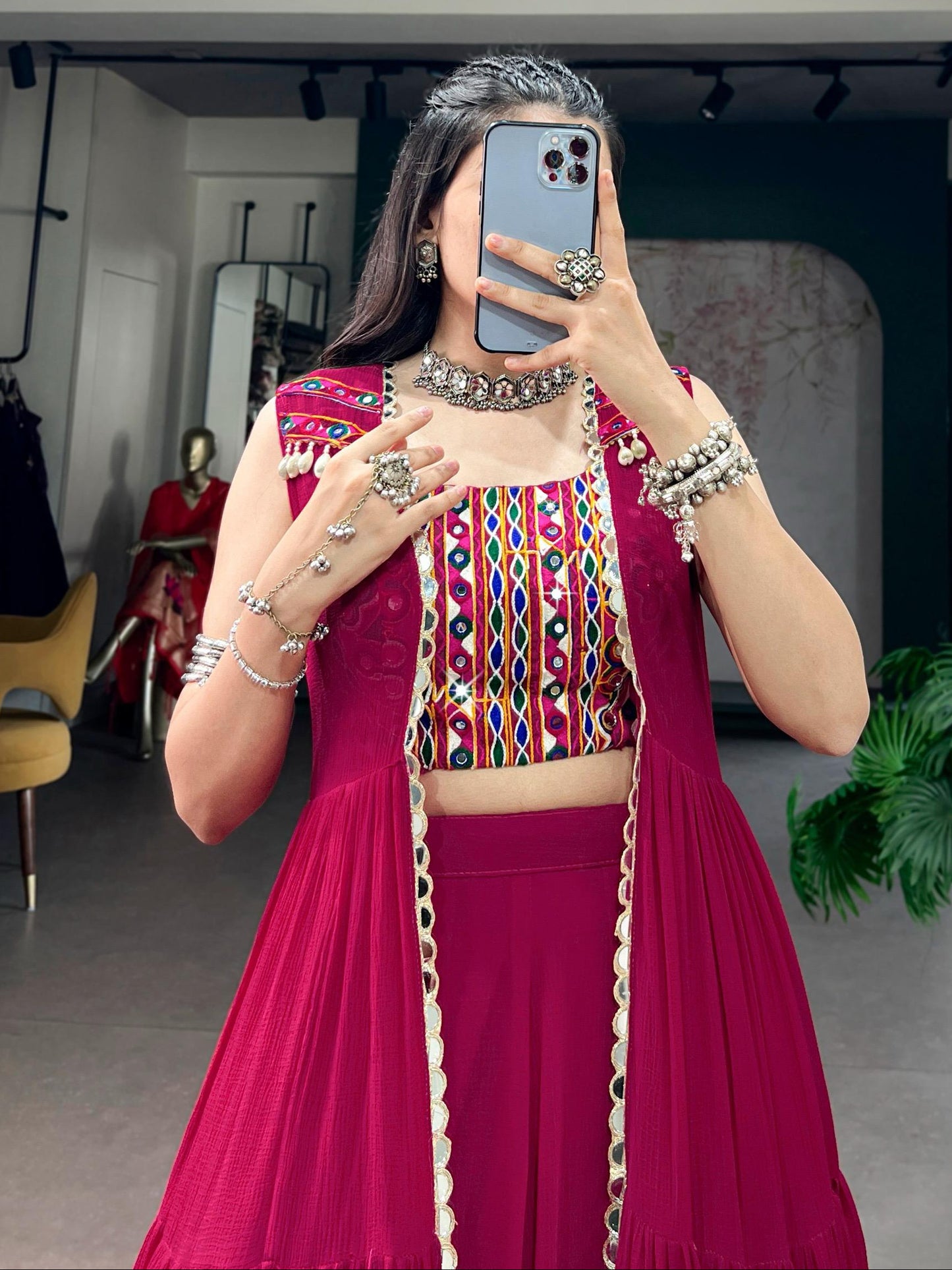 Person taking a mirror selfie wearing a vibrant traditional outfit with jewelry in an indoor setting.