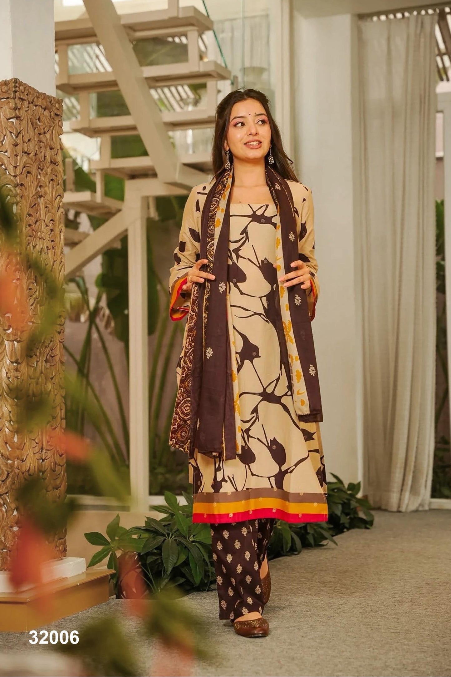 Woman in a patterned outfit standing in a modern indoor setting with plants and architectural elements.