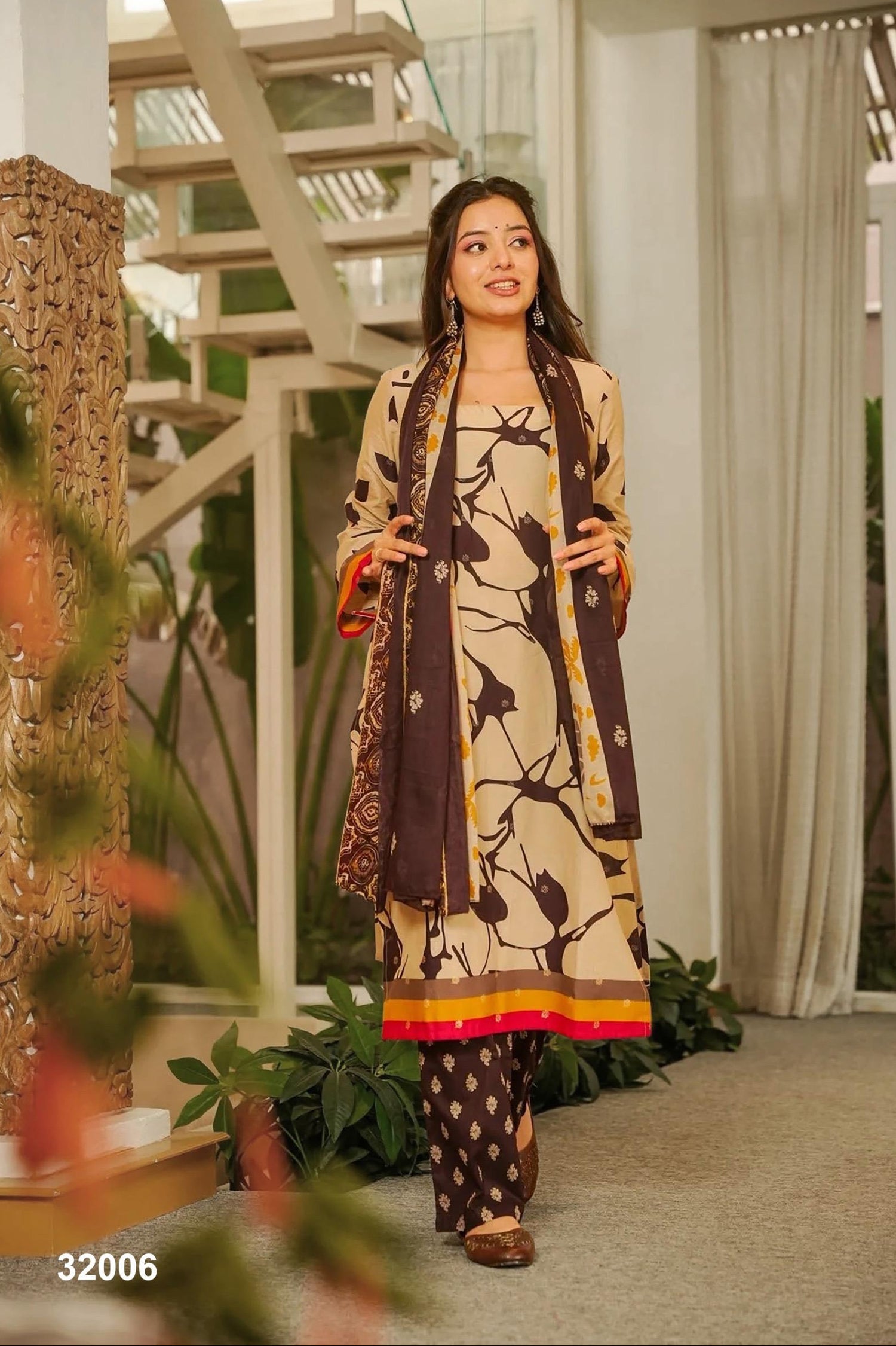 Woman in a patterned outfit standing in a modern indoor setting with plants and architectural elements.