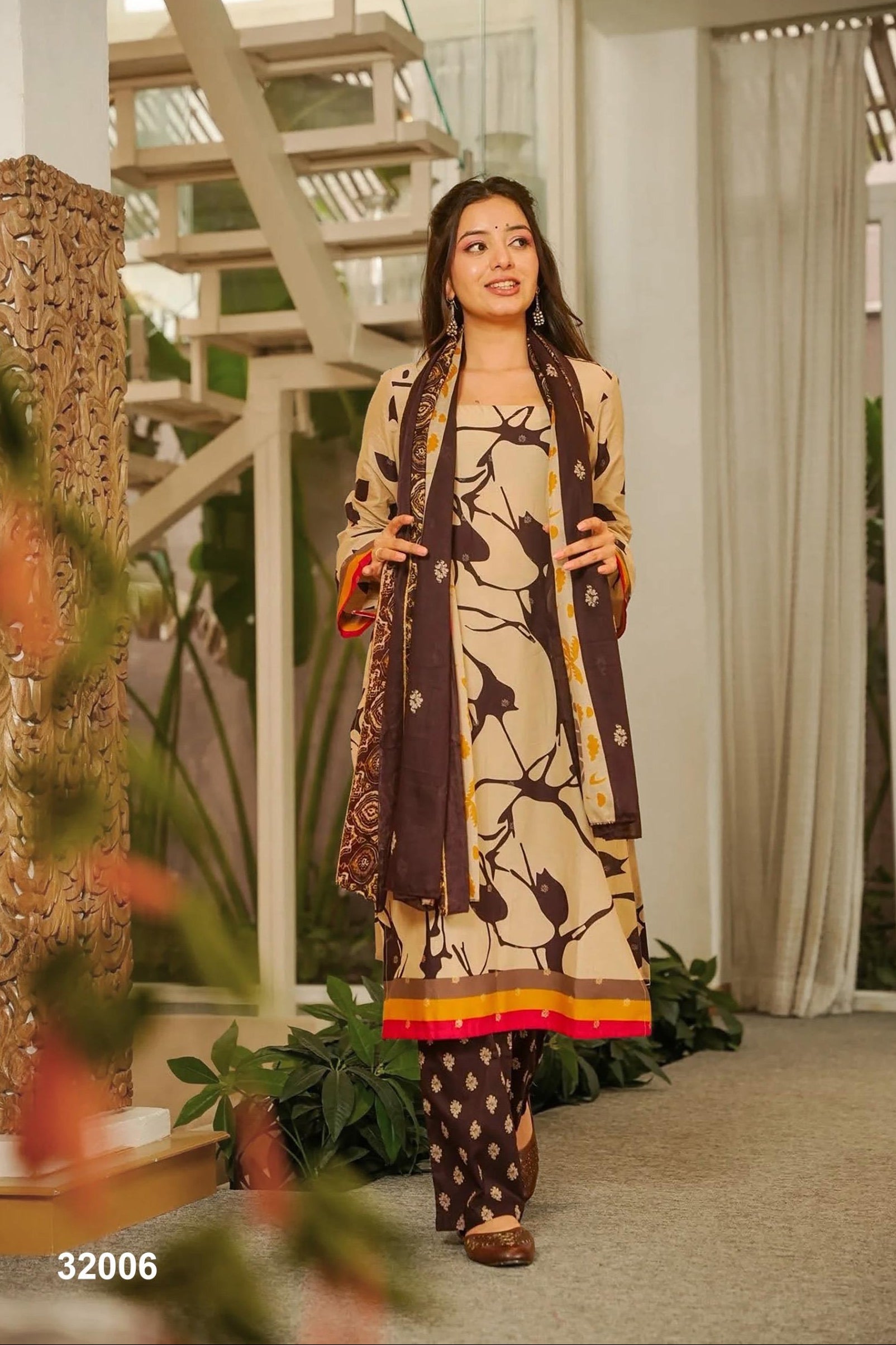 Woman in a patterned outfit standing in a modern indoor setting with plants and architectural elements.