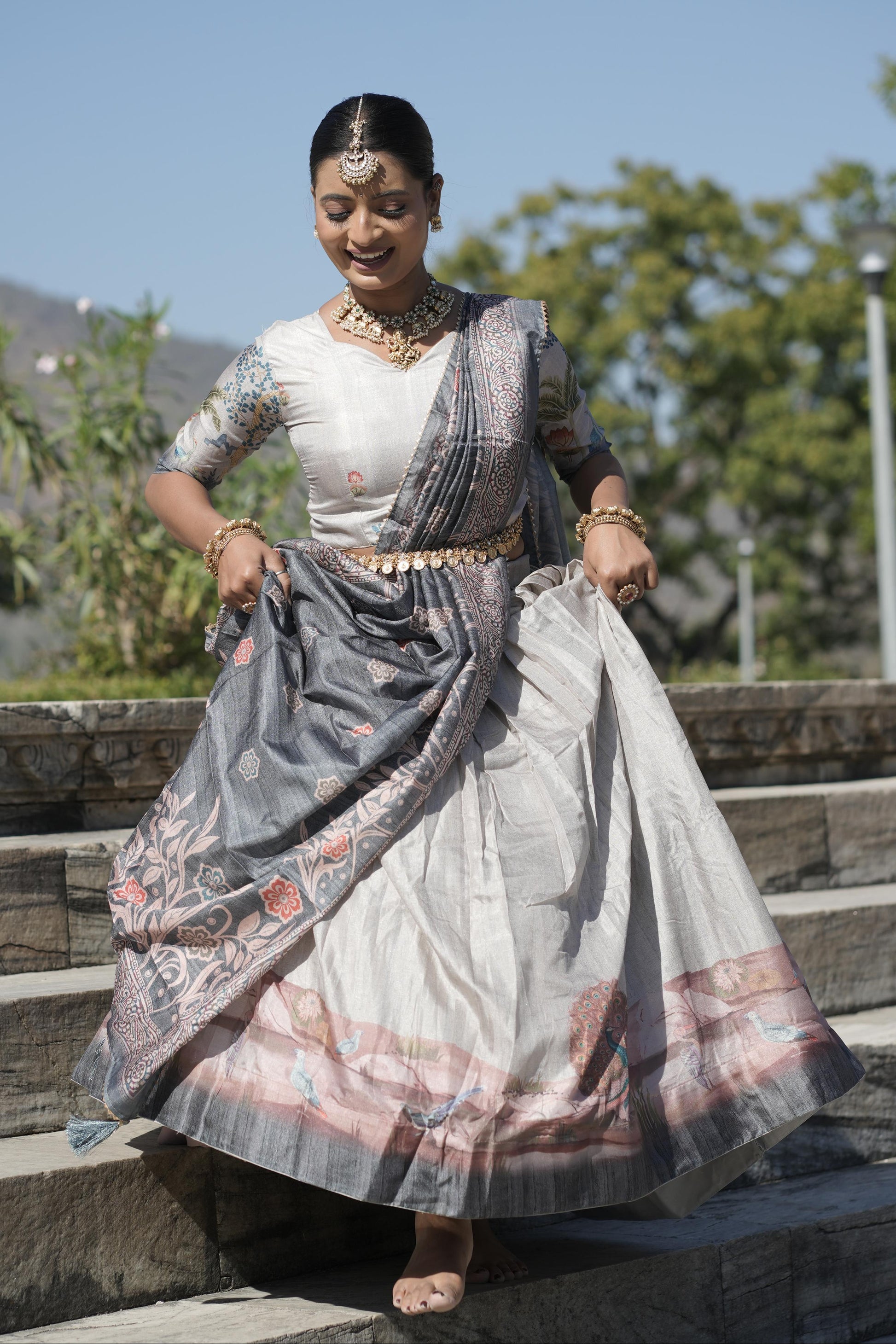 Woman in traditional attire standing outdoors with trees and clear sky in the background