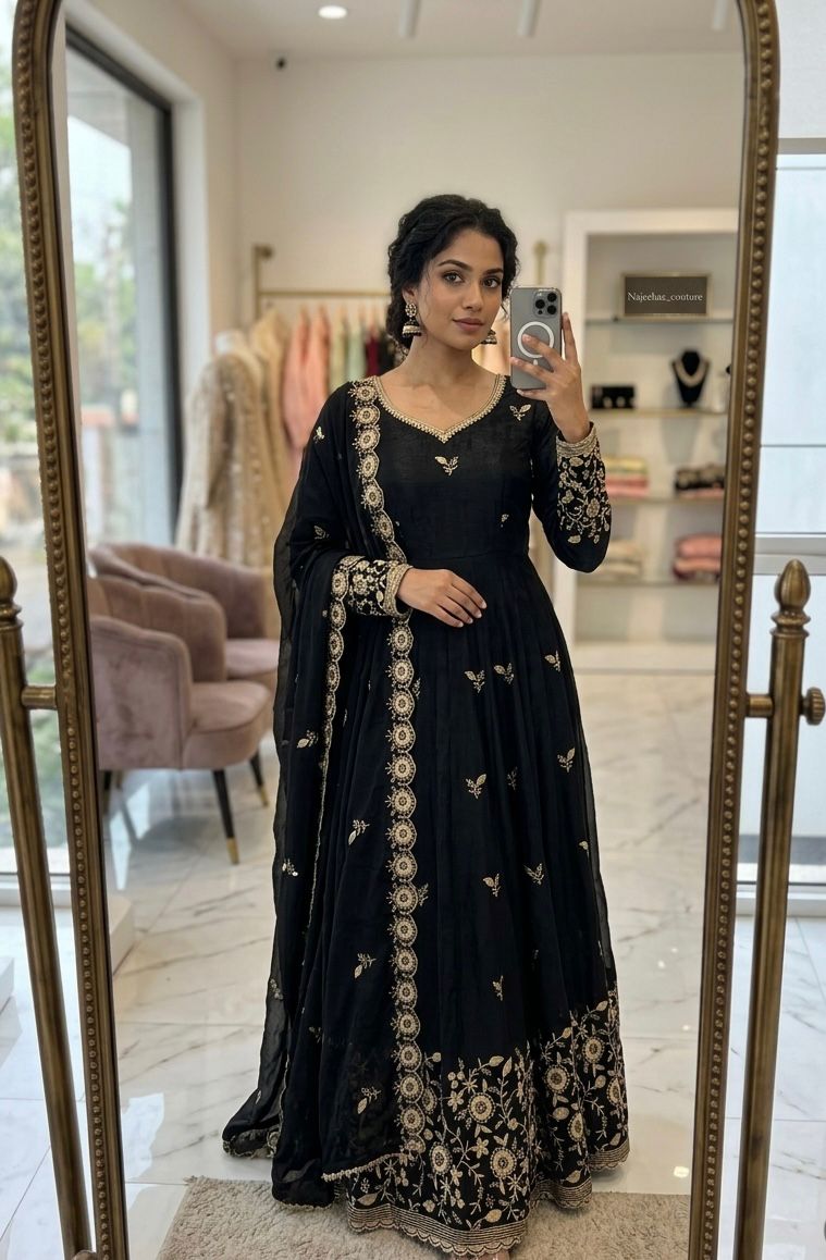 Woman in a black embroidered dress taking a mirror selfie in a store.
