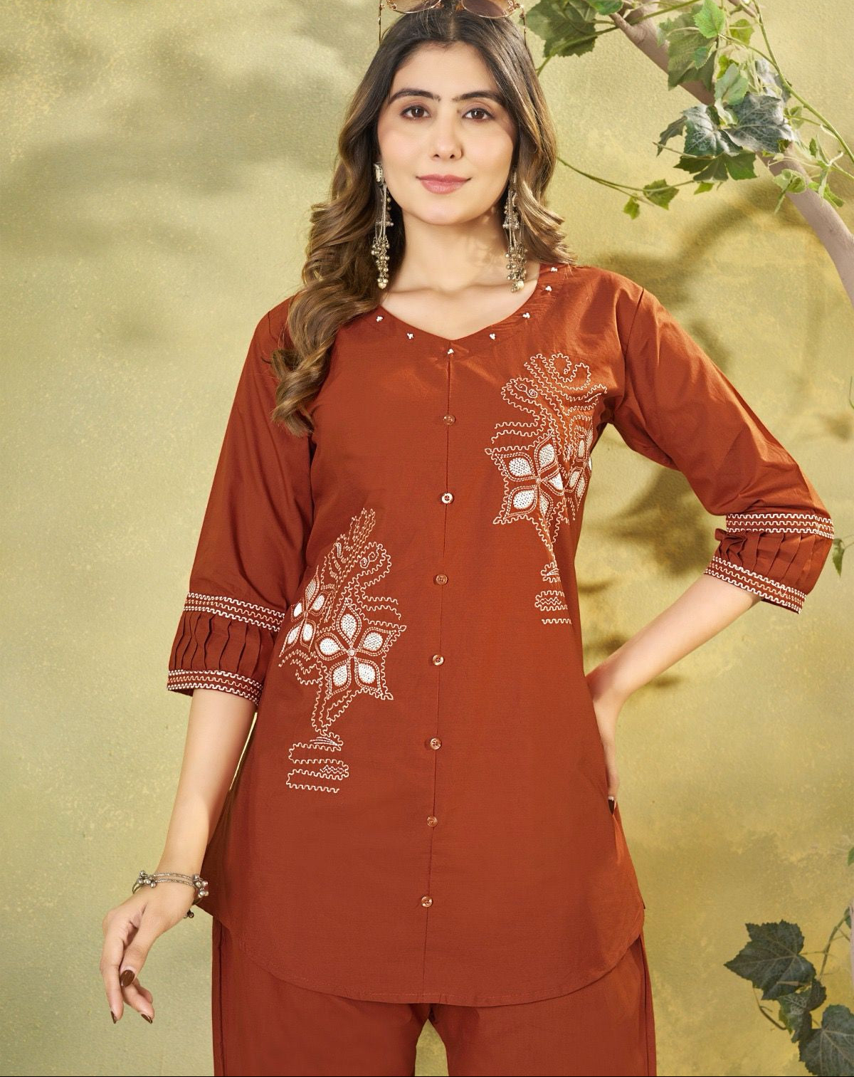 Woman wearing a rust-colored embroidered outfit against a green leafy background
