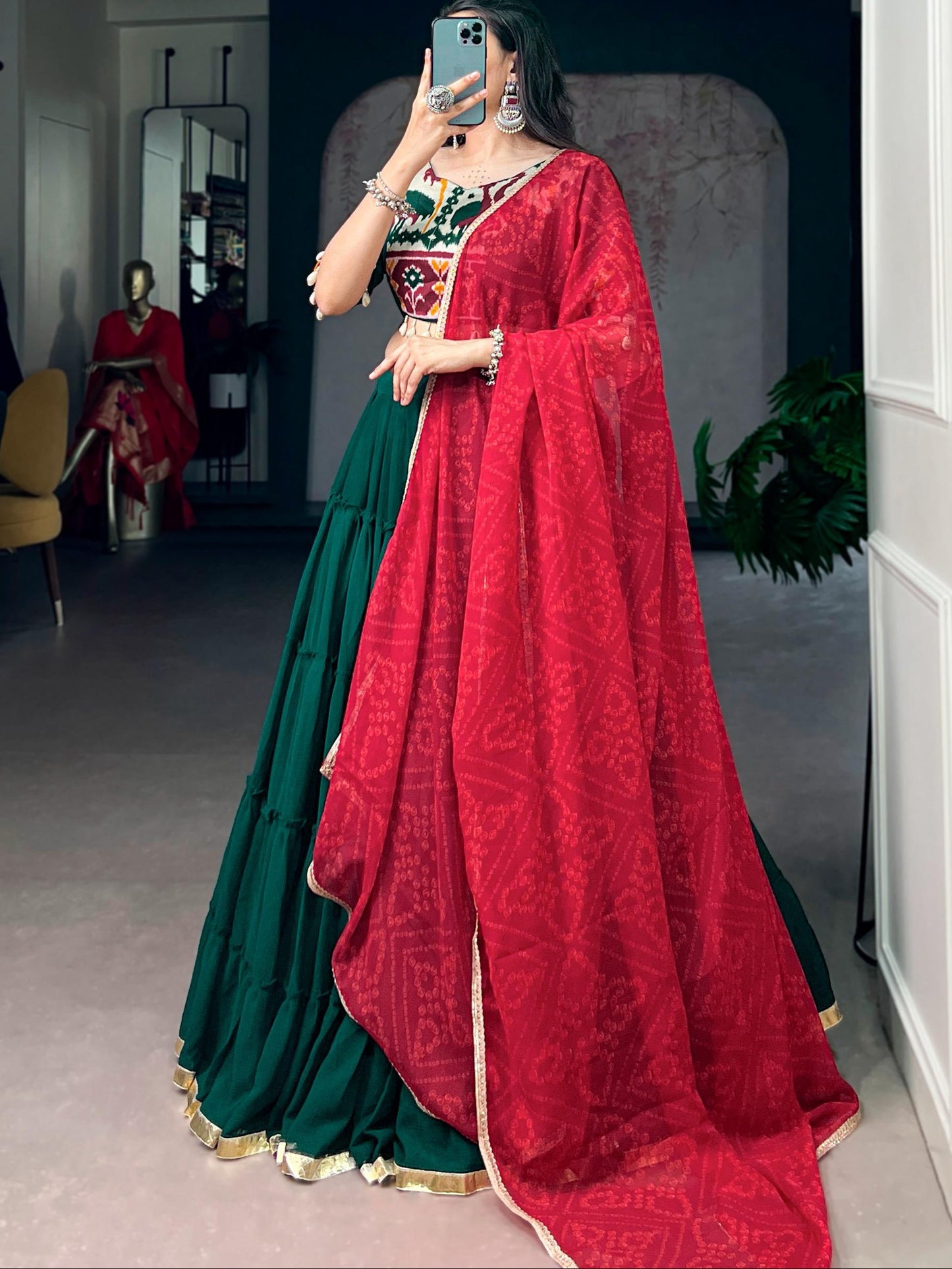 Woman in a green and red traditional outfit taking a mirror selfie.