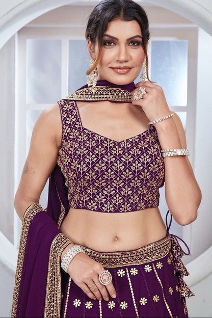 Woman wearing a traditional purple and gold outfit with jewelry indoors.