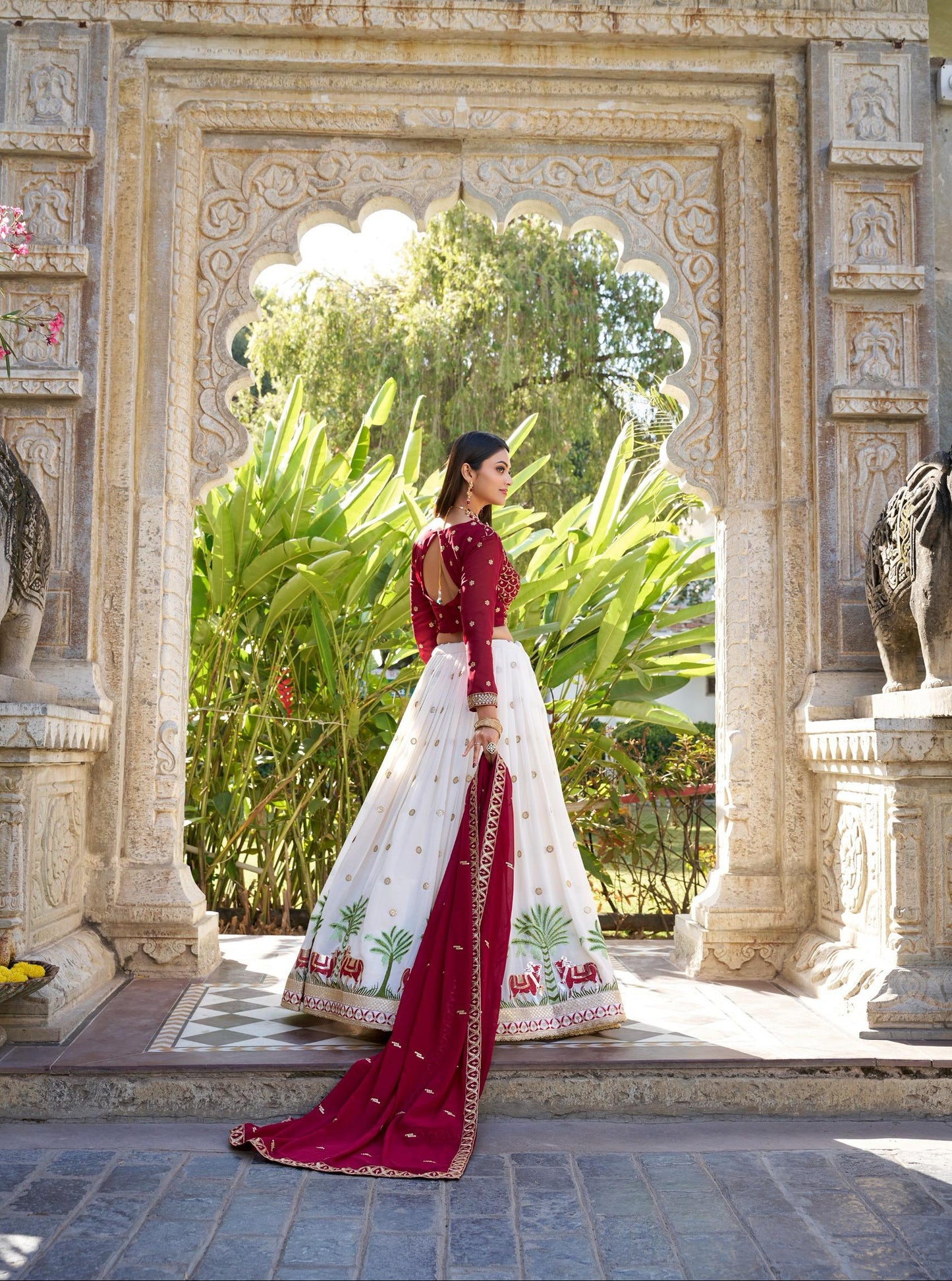 Woman in a red and white traditional outfit standing in front of an ornate stone archway.