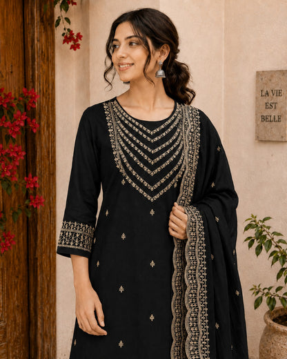 Woman wearing a black traditional outfit with intricate gold embroidery indoors.