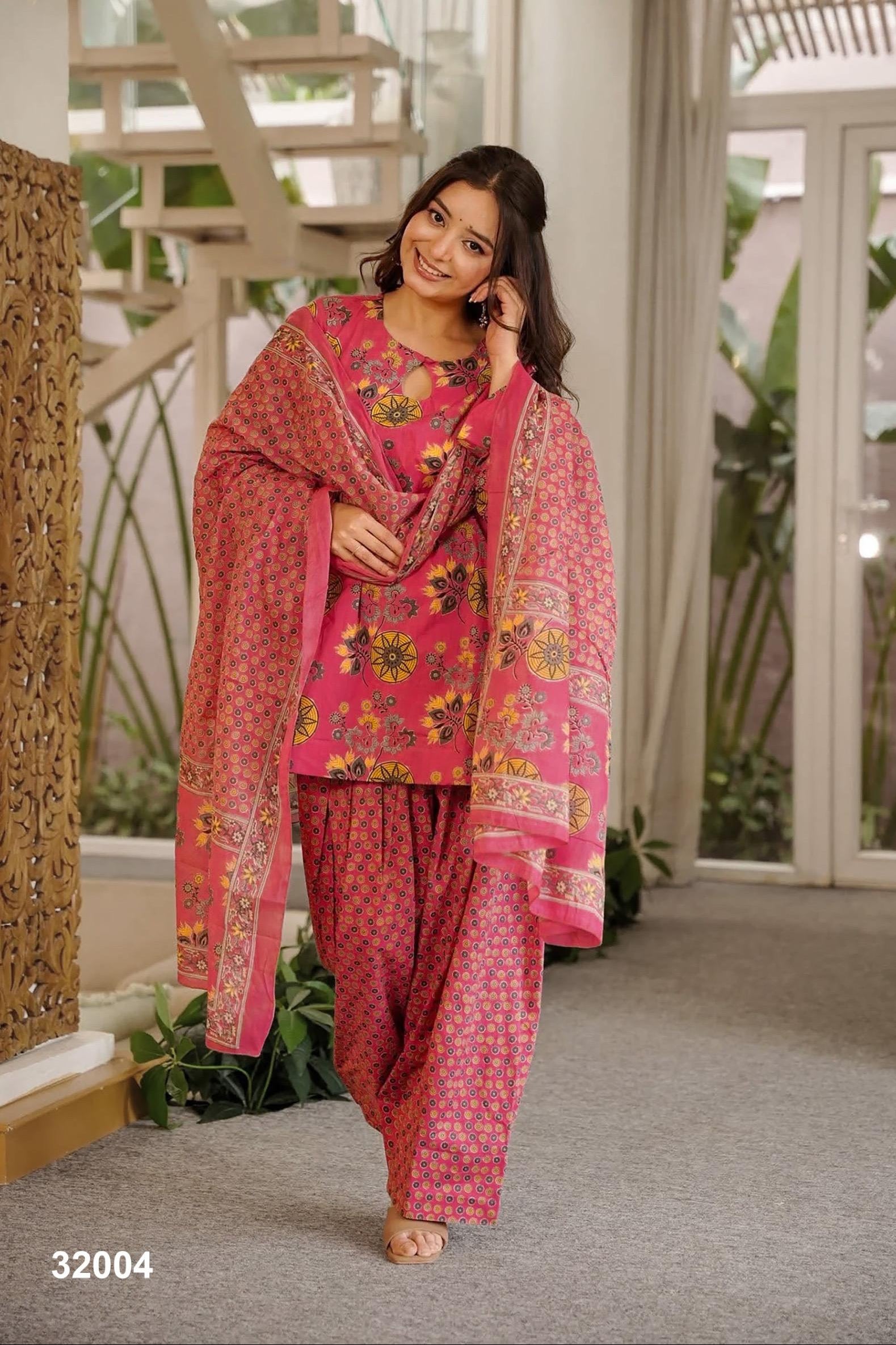Woman wearing a pink traditional outfit with a floral pattern in an indoor setting.