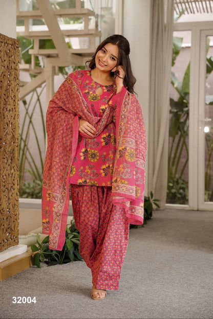 Woman wearing a pink traditional outfit with a floral pattern in an indoor setting.