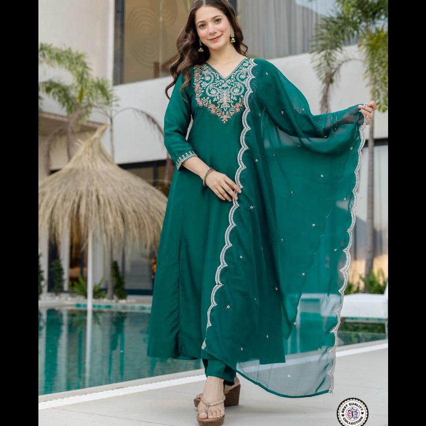 Woman in a teal traditional outfit with embroidery, standing by a poolside.
