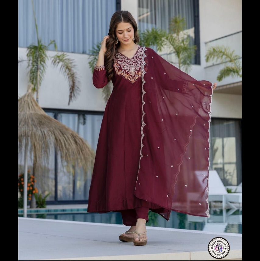 Woman in a maroon traditional outfit with intricate designs standing outdoors.