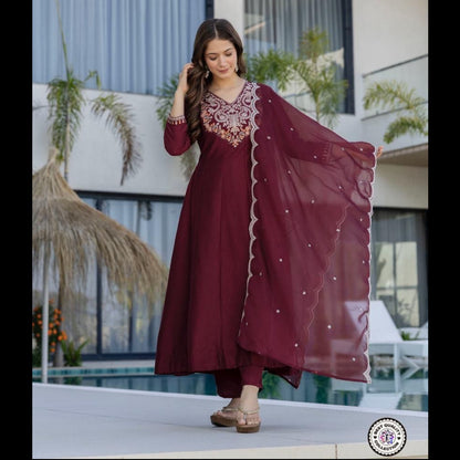 Woman in a maroon traditional outfit with intricate designs standing outdoors.