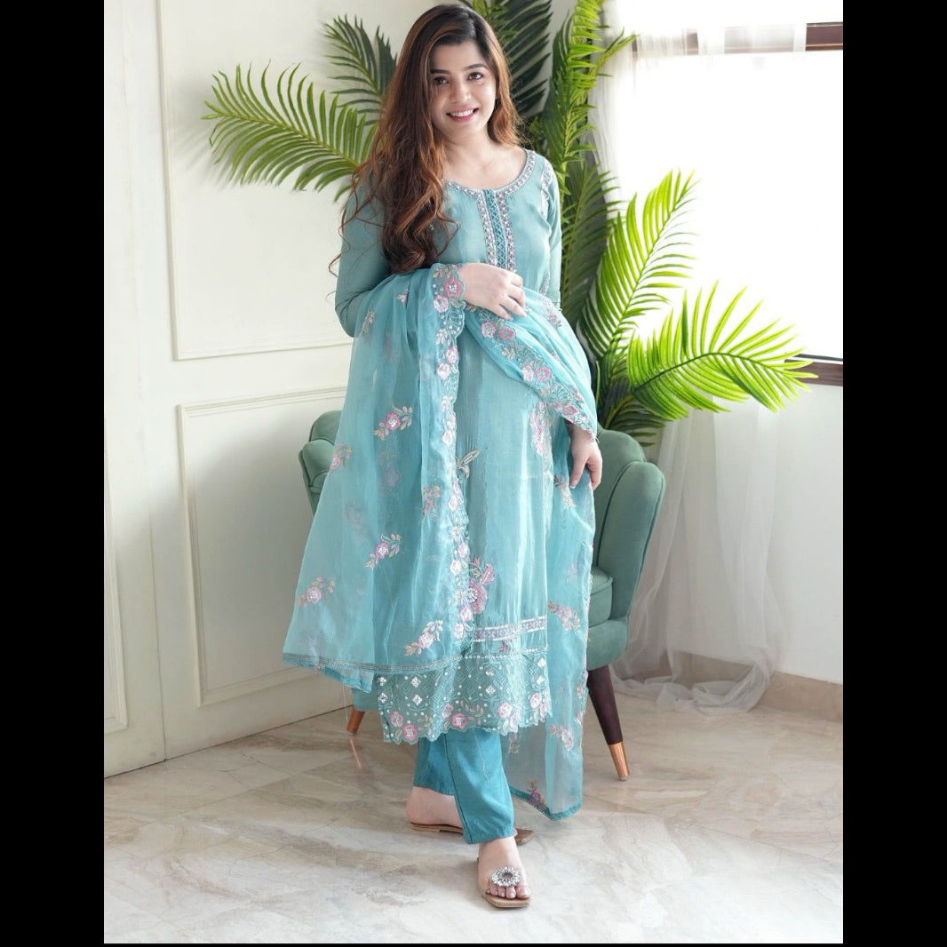 Woman in a light blue embroidered outfit sitting in a room with plants.