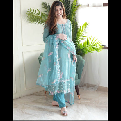 Woman in a light blue embroidered outfit sitting in a room with plants.