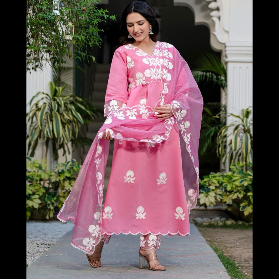 Woman in a pink traditional outfit with white embroidery standing outdoors.