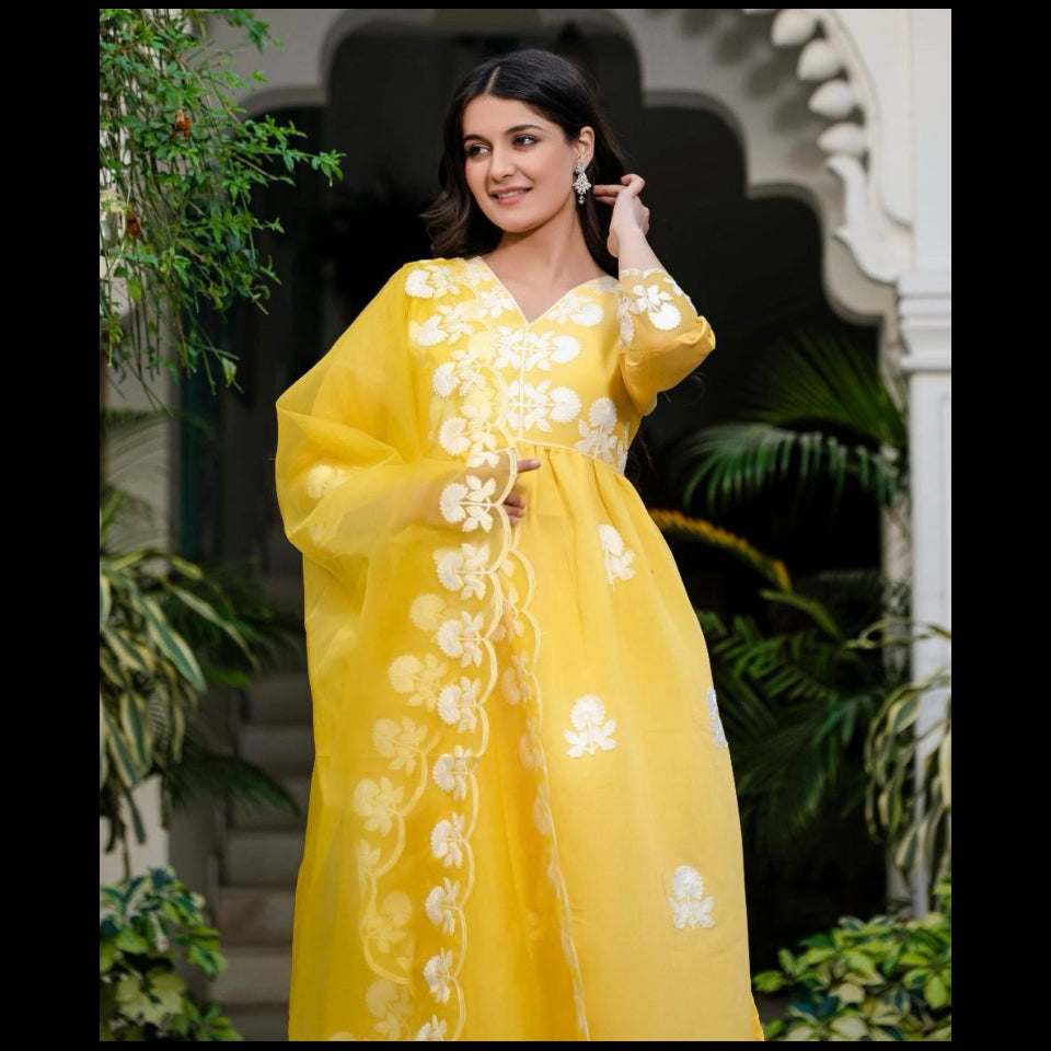 Woman in a yellow dress with white floral embroidery standing outdoors.