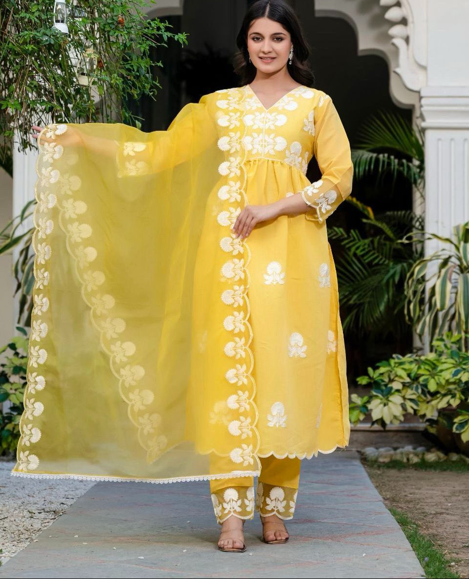 Woman wearing a yellow traditional outfit with white floral patterns in an outdoor setting.