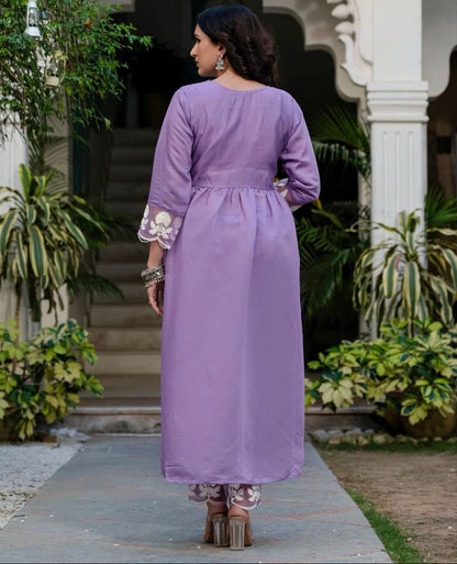 Woman in a purple dress standing in front of an architectural entrance with plants around.