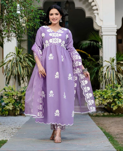 Woman in a purple dress with white floral patterns standing outdoors.