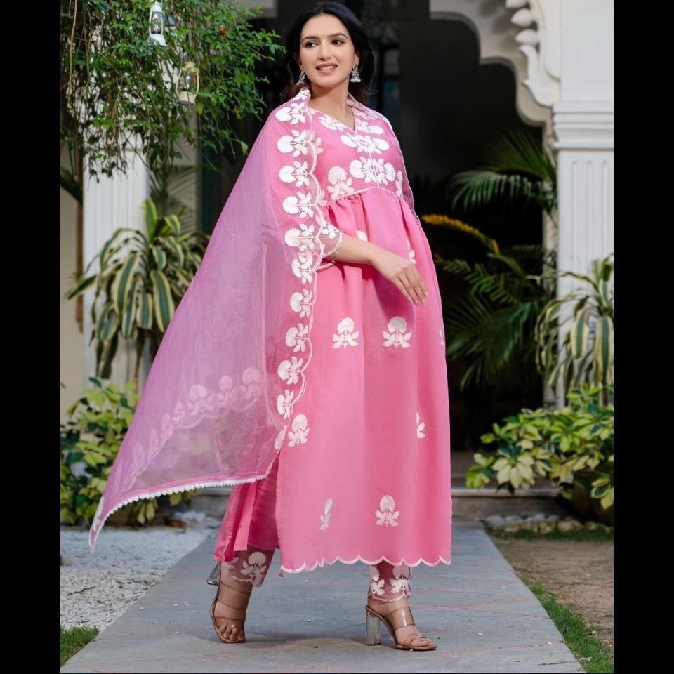 Woman in a pink traditional outfit with white embroidery standing outdoors.