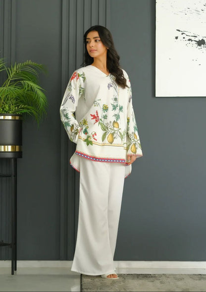 Woman wearing a floral blouse and white pants standing against a gray wall with a plant and abstract art in the background. MARTIVA