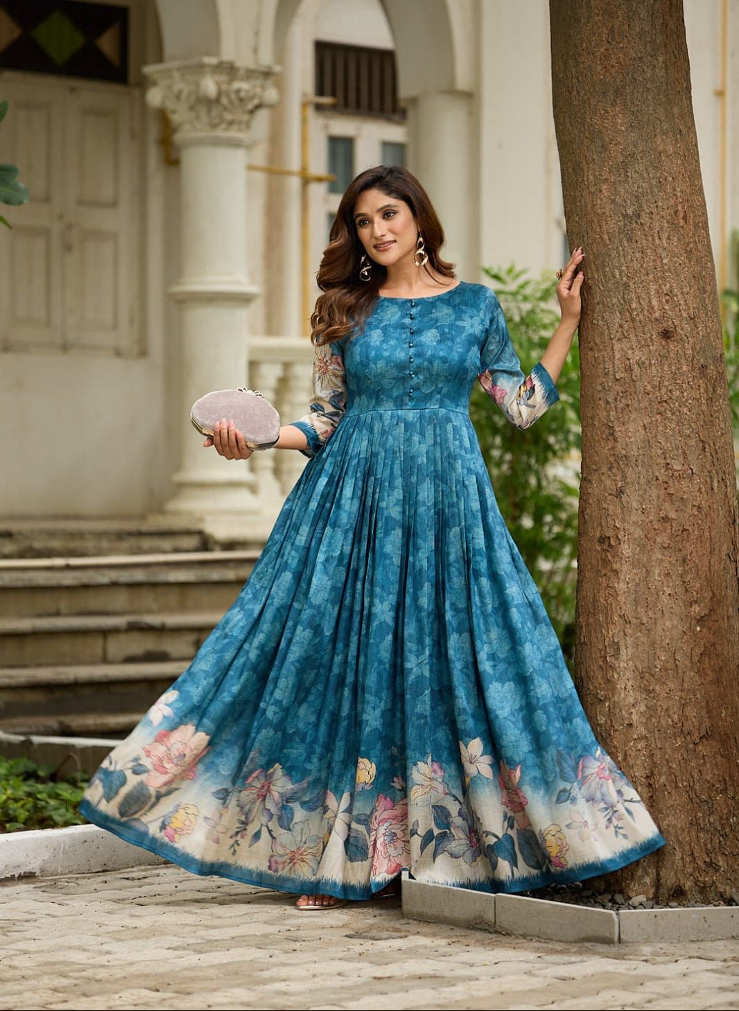 Woman in a blue floral dress standing next to a tree in an outdoor setting