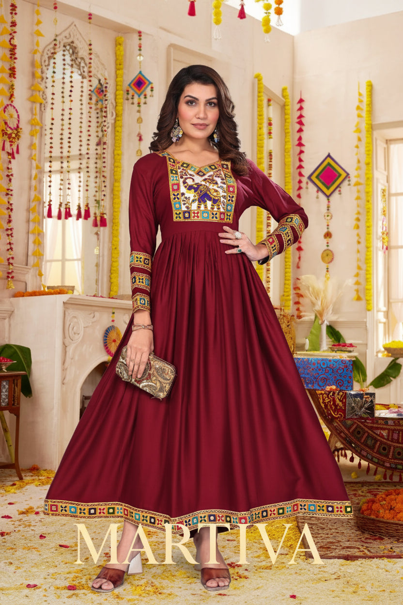 Woman in a maroon traditional dress with colorful embroidery in a decorated room.