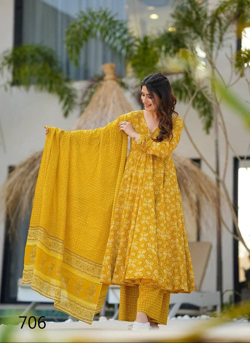 Woman in a yellow traditional outfit holding a dupatta with plants and a building in the background