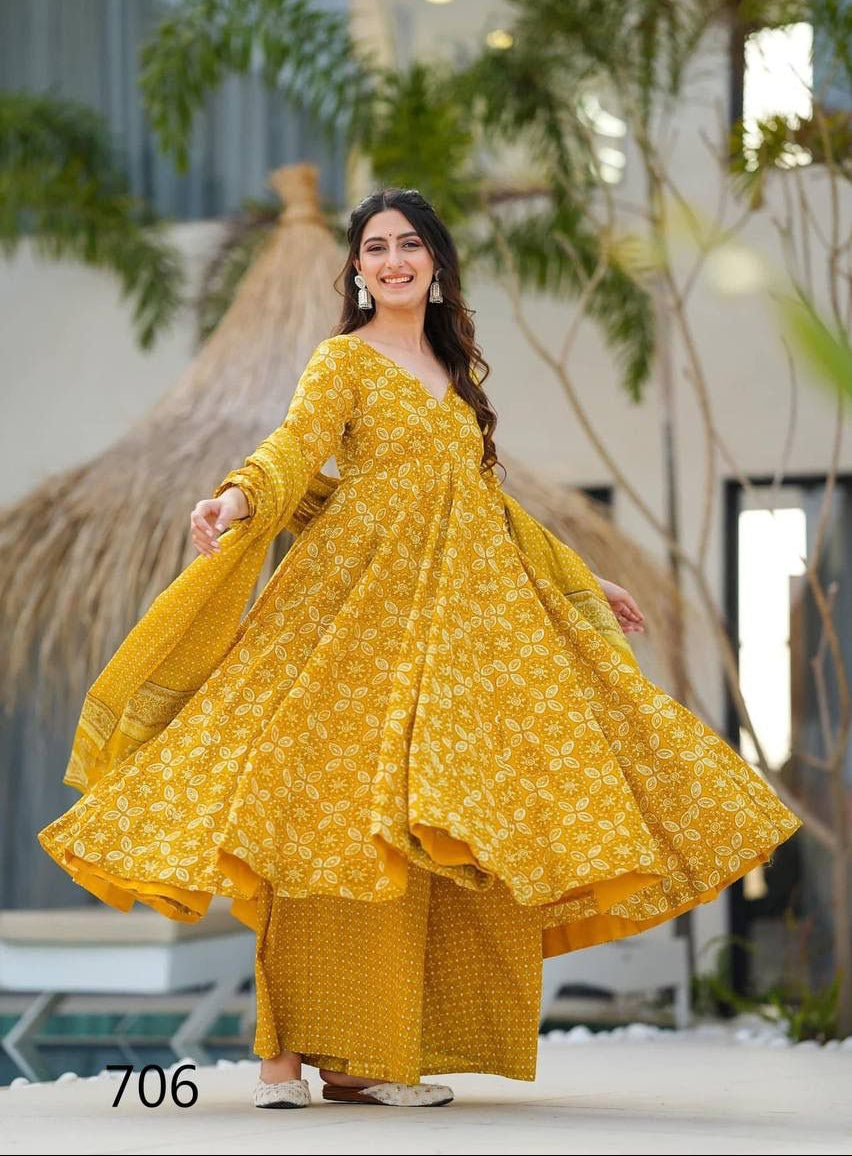 Woman in a yellow traditional outfit standing outdoors with plants in the background