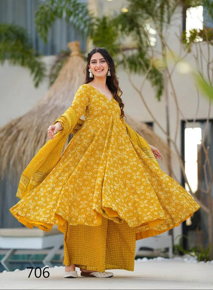Woman in a yellow traditional outfit standing outdoors with plants in the background