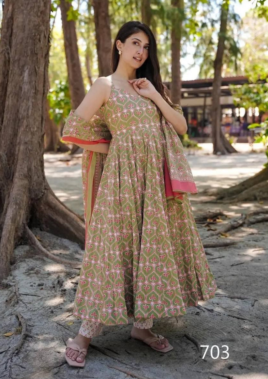 Woman in a patterned dress standing in a natural setting with trees and sunlight.