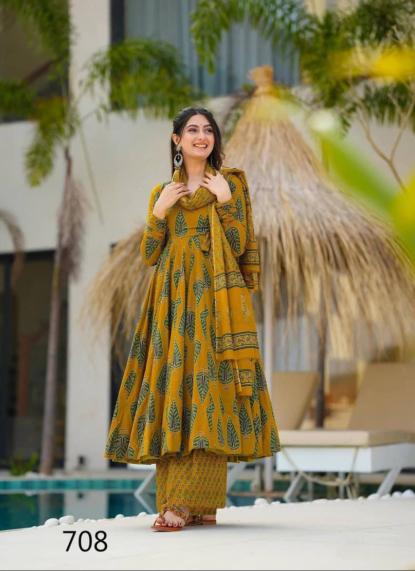 Woman in a yellow traditional outfit standing by a poolside with greenery and a thatched umbrella in the background.