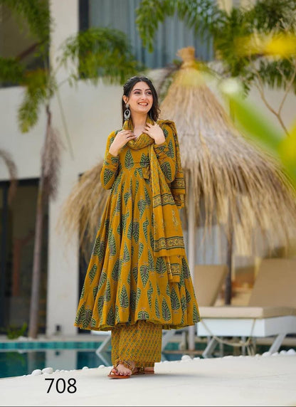Woman in a yellow traditional outfit standing by a poolside with greenery and a thatched umbrella in the background.