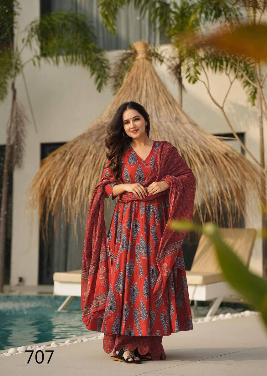 Woman in a red and blue patterned dress standing by a poolside with a thatched roof structure in the background.