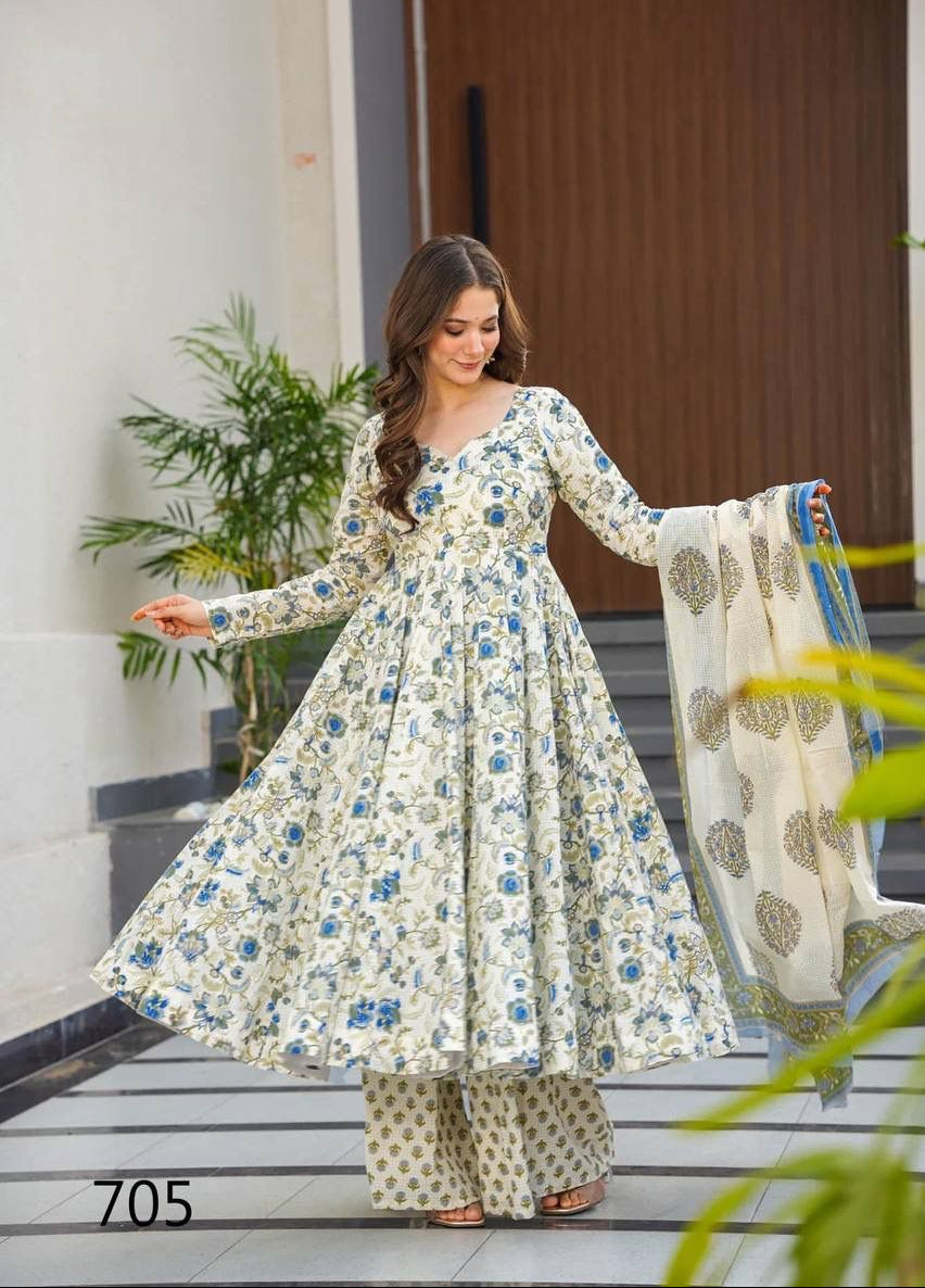 Woman in a floral dress holding a dupatta on a steps with plants in the background
