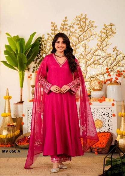 Woman in a pink traditional outfit standing in a decorated room with plants and decorative items.