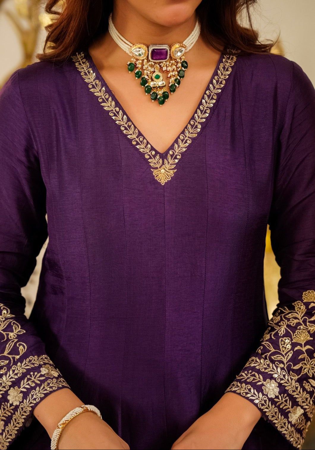 Purple outfit with gold embroidery and a necklace with green and purple stones.
