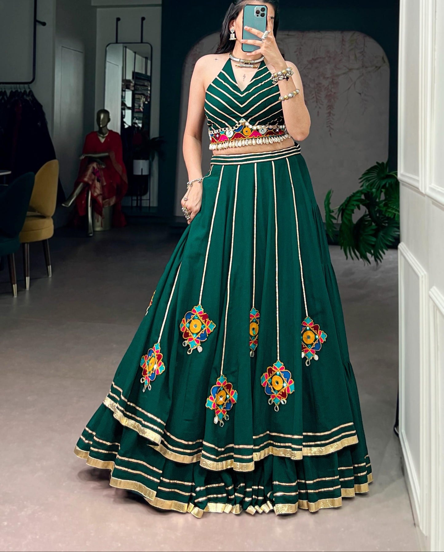 Woman wearing a green embroidered dress taking a mirror selfie in a room.