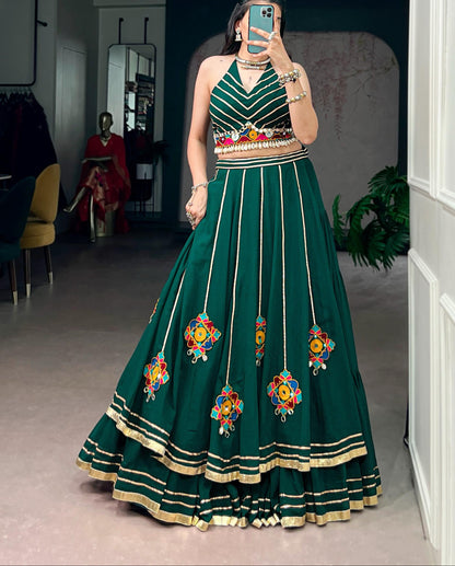 Woman wearing a green embroidered dress taking a mirror selfie in a room.