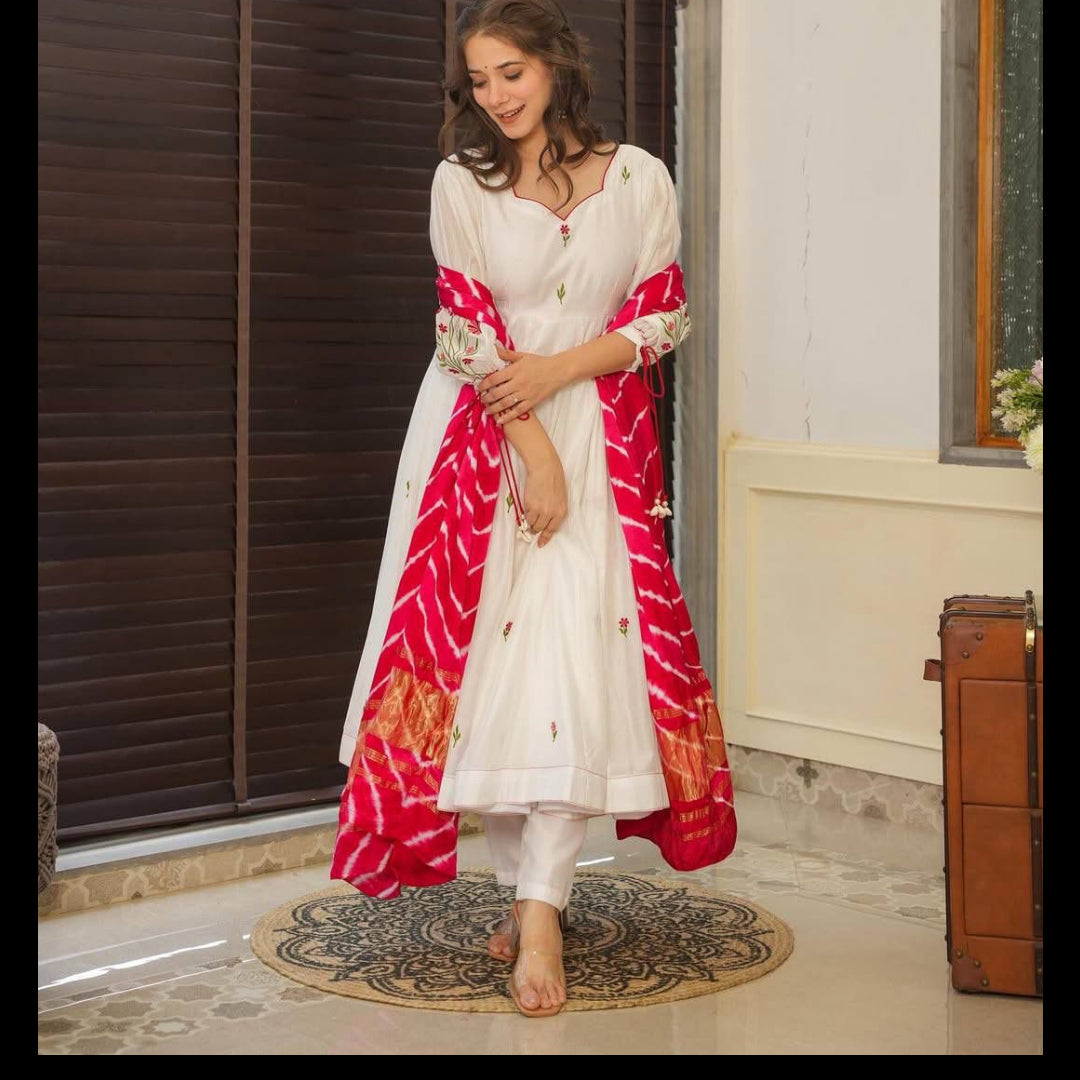 Woman wearing a white outfit with a red and pink patterned scarf indoors.