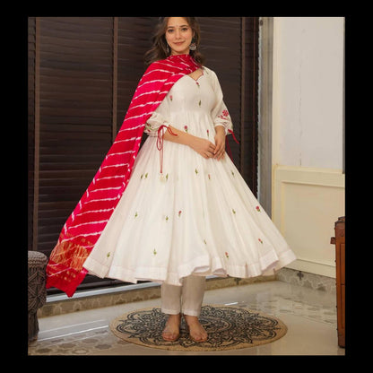 Woman in a white embroidered anarkali suit with a red dupatta standing indoors.